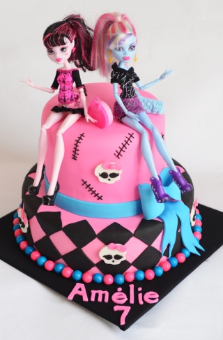 Gâteau sous le thème de ''Monster High'' pour une princesse de 7 ans! L`intérieur du gâteau est trois couleurs (vanille, chocolat, vanille rose) avec un glaçage crème au beurre à la vanille entre chaque couche. Il est recouvert de fondant et décoré avec deux barbies ''Monster High''.