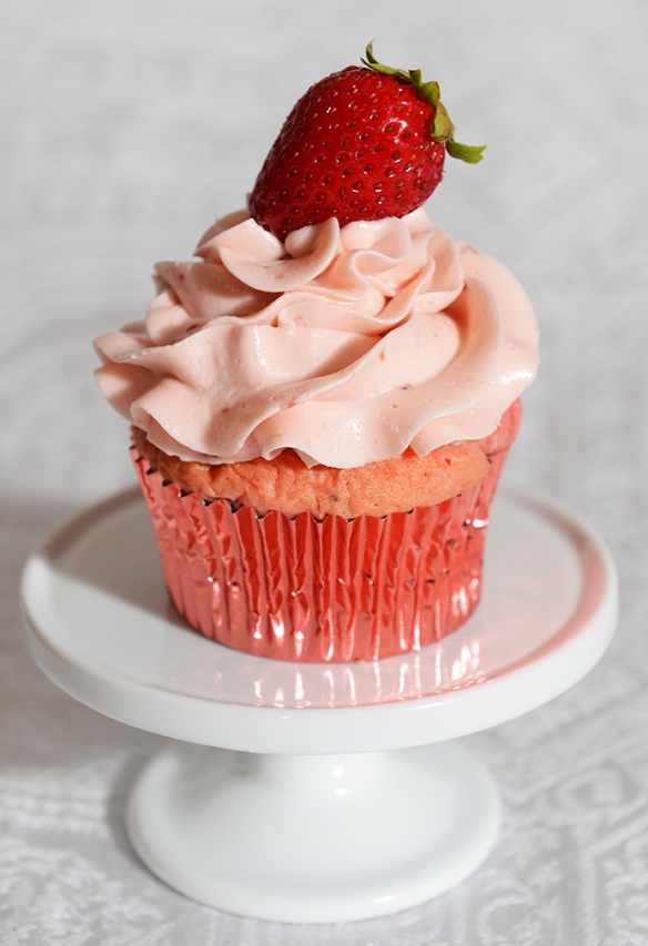 Cupcake rose à la fraise avec glaçage meringue suisse aux fraises et garnis d'une fraise fraîche.